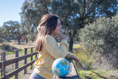 Obraz na plátně Young girl contemplating a globe in a natural outdoor environment, reflecting on