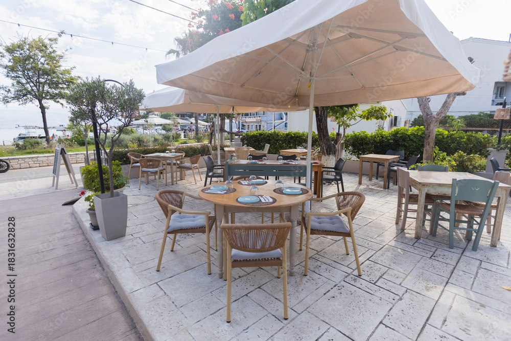 Fototapeta premium Modern outdoor cafe table with wicker chairs and green plants