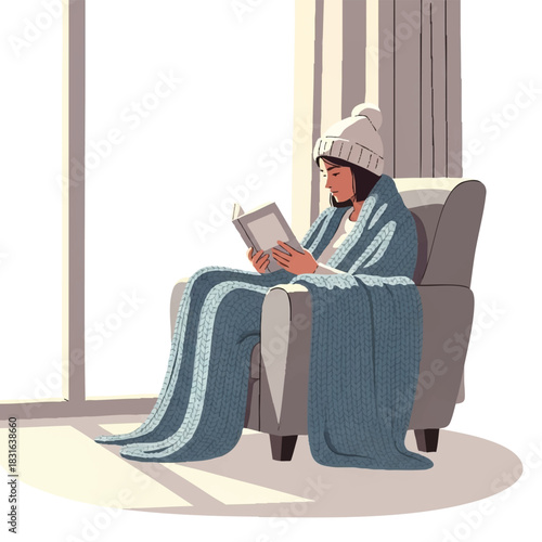A woman wearing a knit hat and wrapped in a blue blanket sits in a chair reading a book by a sunny window with a curtain.