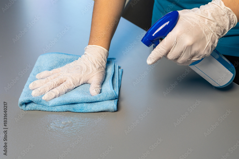 Fototapeta premium Close up of female hand wiping table with cloth. Concept of home cleaning, hygiene, surface care, household chores. Suitable for housekeeping and cleaning service themes.