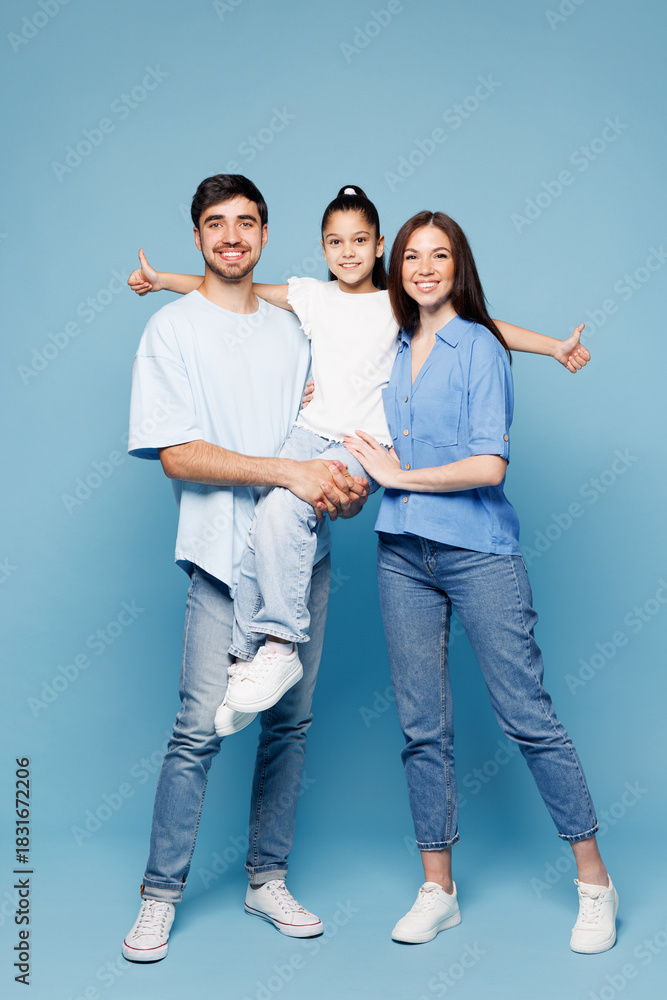 Obraz premium Full body young smiling fun happy parents mom dad with child kid girl wearing casual clothes hold daughter in hands look camera hugging isolated on plain blue background. Family day childhood concept.