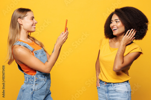 Side view two young friends buddies women wear casual clothes together taking photo shot on mobile cell phone post photo on social network isolated on plain yellow orange background Lifestyle concept