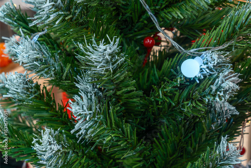 Snowy artificial christmas tree with lights and red berries. Winter holiday tree with artificial snow white led lights and vibrant red berry accents for festive interior.