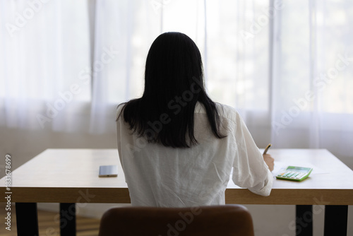 Back View of Woman Working at Desk with Pen in Hand