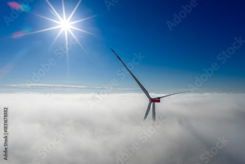 Принти на полотні A wind turbine rises through a dense cloud layer, with the bright sun shining above the clear sky