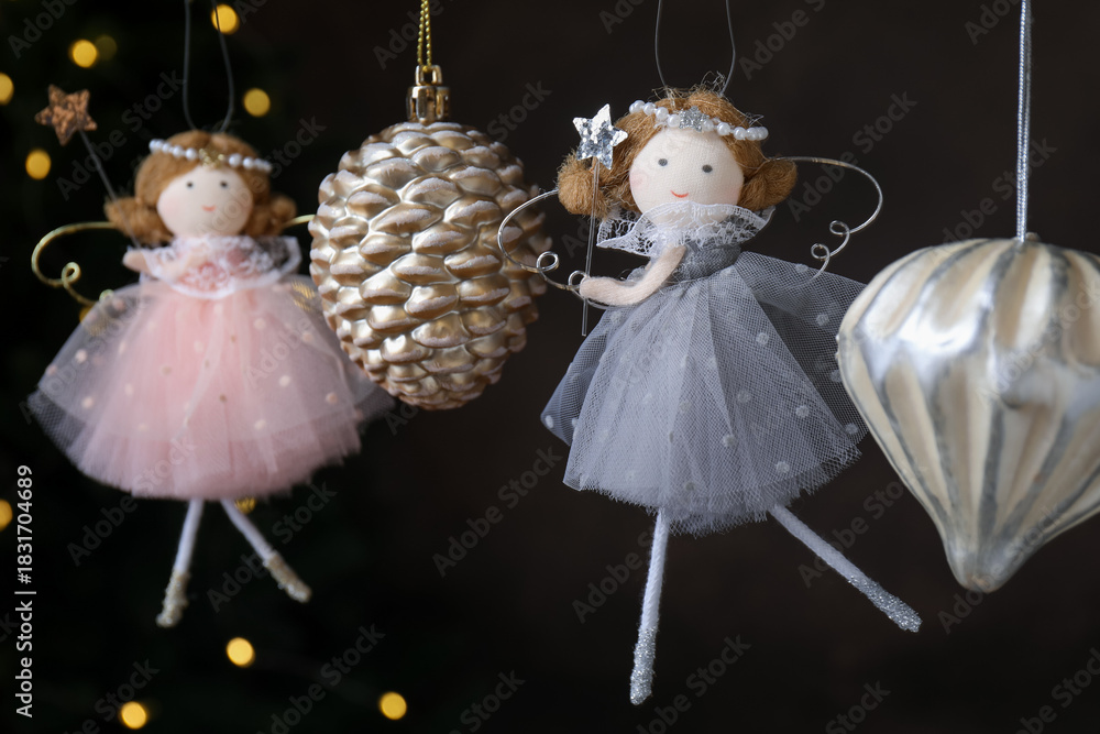Fototapeta premium Beautiful Christmas decor and fairy dolls hanging against black background with blurred lights, closeup