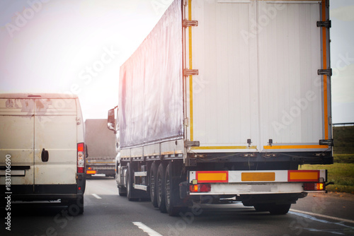 Rear view of truck trailer and delivery van on highway. Road transport and logistics concept during daytime with bright sky