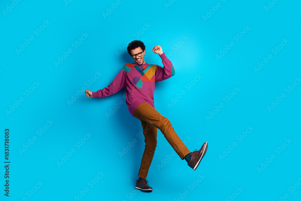 Obraz premium Happy young man in stylish casual outfit dancing against vibrant blue background, showcasing joyful and energetic expression
