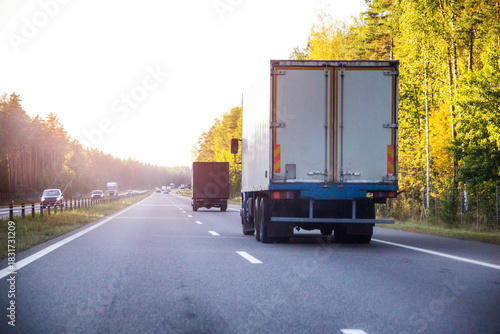 Fototapeta Naklejka Na Ścianę i Meble -  A refrigerated truck transports perishable food cargo along a highway in summer against a sunset backdrop, industry. Copy space for text