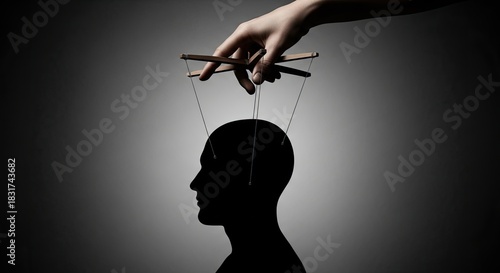 Silhouette of a mans head being controlled by puppet strings held by a hand, symbolizing manipulation, control, and the loss of free will and autonomy