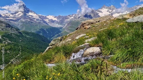 Close-up of crystal clear mountain stream with audio. Fresh green grass and snowy peaks of Matterhorn in background, Zermatt, Switzerland. 4K cinematic nature soundscape. Alpine spring aesthetics.