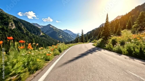 Scenic mountain road winding through lush green landscape with wildflowers and sunlight