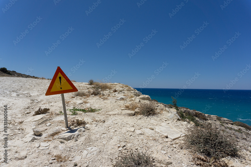 Fototapeta premium Segnale stradale di pericolo, forma triangolare, giallo e rosso con punto esclamativo, sulla scogliera bianca di Kalamaki , isola di Creta