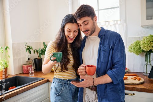 Young couple having morning coffee at home using mobile phone together