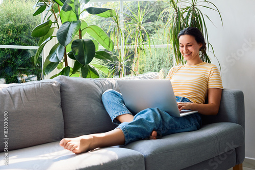Smiling young woman using laptop sitting relaxed on a sofa at home