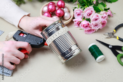 Florist at work: woman shows how to make modern Christmas decoration with fir, roses, pink baubles and decorative stars. The base is classic can. Step by step, complete tutorial.