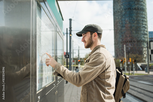 Young man checking public transport map at station in urban city