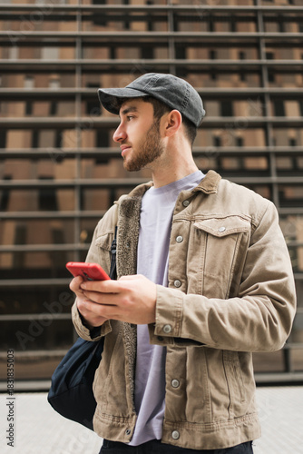 Young man standing in urban area holding smartphone and looking sideways