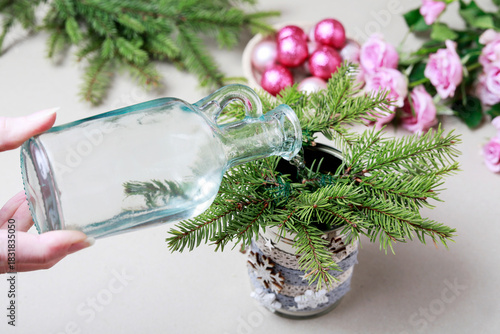 Florist at work: woman shows how to make modern Christmas decoration with fir, roses, pink baubles and decorative stars. The base is classic can. Step by step, complete tutorial.