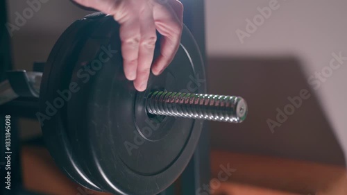 Additional weight is being loaded onto the barbell, close-up. Tightening the barbell screw