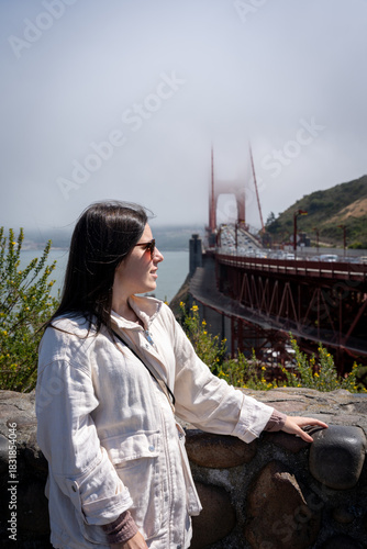 Stylish Woman with Sunglasses Looking Away by Golden Gate Bridge on a Foggy Day