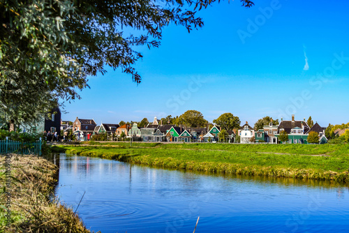 Peaceful Dutch landscape with a calm canal and historic architecture under a clear blue sky.