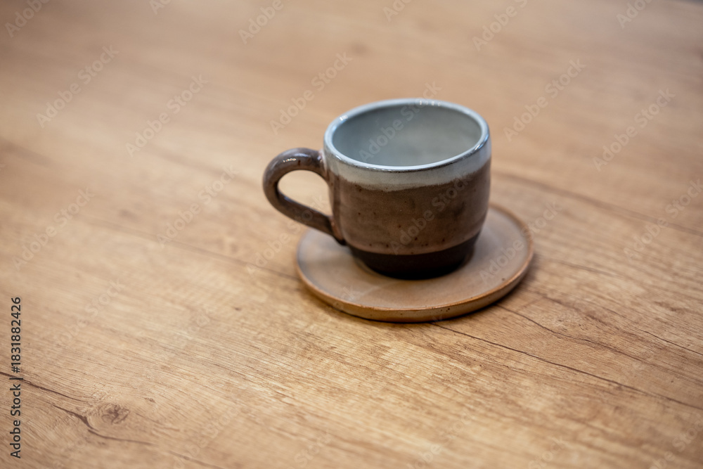 Obraz premium Handmade ceramic coffee cup with saucer on a wooden table. Simple clay design with glazed surface.