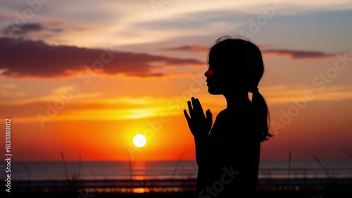 Silhouette of a young girl praying at sunset by the ocean, creating a serene and spiritual atmosphere