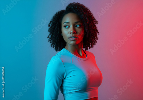 Young Black woman athlete looking away with confident expression in studio, illuminated by dramatic cyan and red neon dual gel lighting