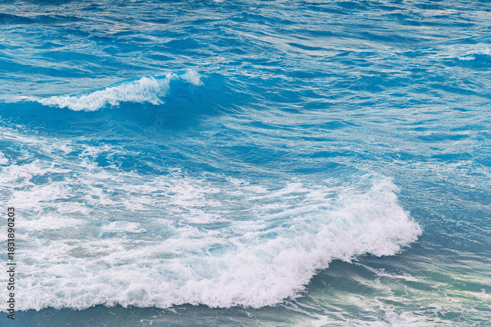 Obraz premium Vibrant ocean waves crashing against the shore on a sunny day