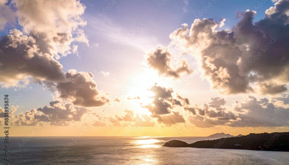 Fototapeta premium A beautiful sunset over the ocean, with dramatic clouds and an island in the distance. The sun is shining brightly, creating a warm and inviting atmosphere.