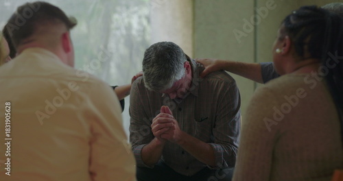 Photography Man bows head and clasps hands during group therapy session while surrounded by
