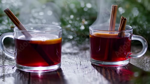 Two warm mugs of spiced drink, steaming, with cinnamon sticks and lemon slices