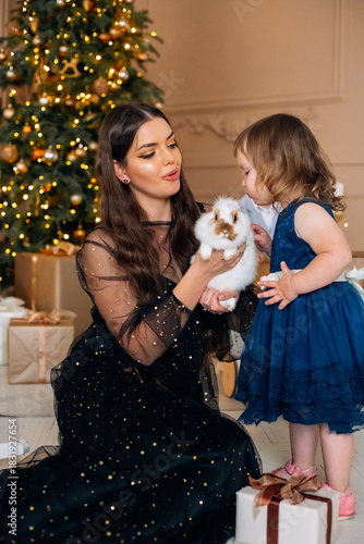 Mother and daughter celebrate Christmas morning together with a puppy and gifts by the decorated tree in a warm family setting