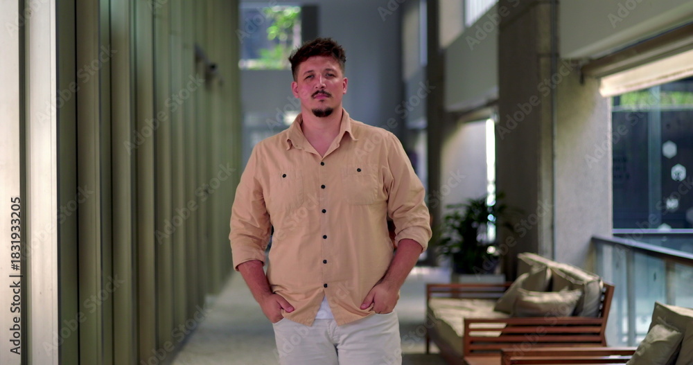 Fototapeta premium Man standing in office hallway with clenched fists and determined expression, posed in modern corridor with seating area in background