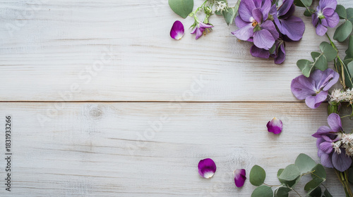 Purple flower petals and green leaves arranged on white wooden background creating calm and natural atmosphere
