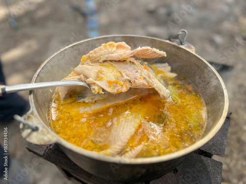 Outdoor cooking fish soup in cauldron over fire