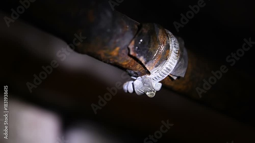 Water drips from under the clamp of a rusty metal pipe. A plumber inspects the water pipes in the basement.Looping.Endless.