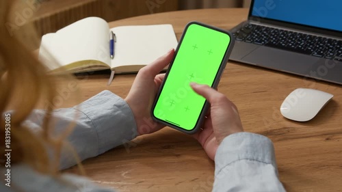 Woman sit use digital tech cell phone, green screen mock up. Hand scroll phone web site, swipe like photos. Girl hold mobile closeup. Chroma key page. Cozy office background. Online app copy space.