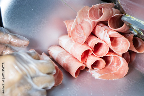 Thinly sliced raw pink meat (pork or beef) rolled up, freshly cut by a meat slicer machine, ready for hot pot or shabu-shabu.