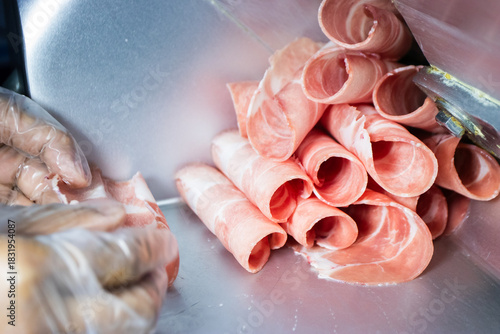 Thinly sliced raw pink meat (pork or beef) rolled up, freshly cut by a meat slicer machine, ready for hot pot or shabu-shabu.