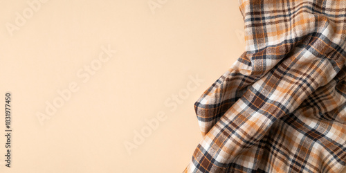 Wrinkled in folds plaid brown orange flannel cotton fabric on beige plain background, top view. Autumnal natural fabric for shirt, dress, tablecloth, clothing. Abstract textile background, tartan 