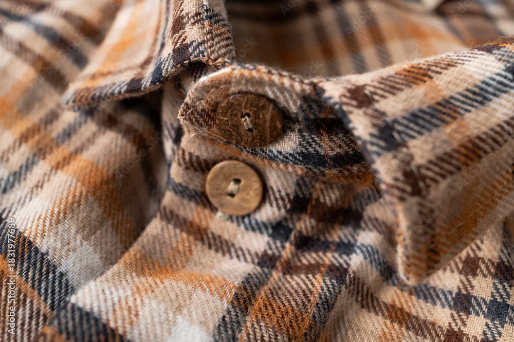 Obraz premium Close-up of plaid shirt detail. Brown and orange cotton flannel shirt, details of the collar, sleeves, pockets, coconut buttons. Clothing texture, tartan pattern. Autumn winter casual shirt