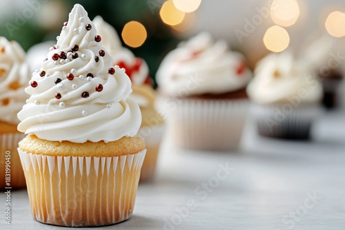 Vanilla christmas cupcake with tall white frosting, decorated with silver pearls and red sprinkles, in an assortment with bokeh lights. Sparkling and elegant holiday dessert concept