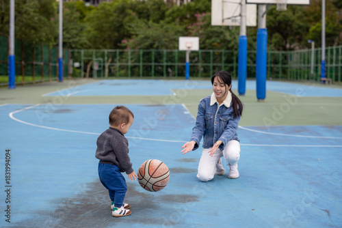 Mother playing basketball with baby at court