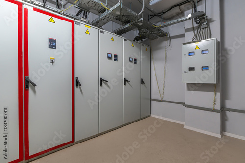 This utility room contains several electrical cabinets with warning signs, control panels, and wiring, showcasing organized equipment in a modern facility setting.