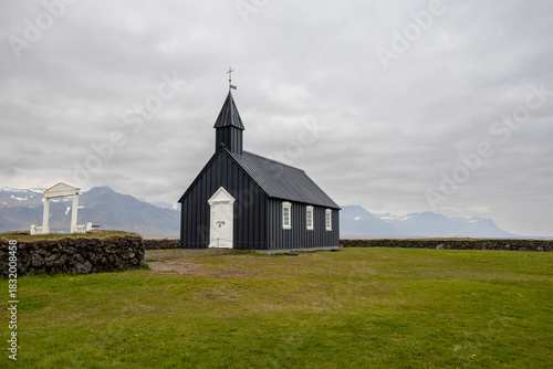 The black wooden church of Búðakirkja with white gate and windows and stone fence, Snaefellsnes peninsula, Iceland