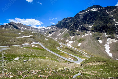 High alpine switchbacks on the Timmelsjoch winding pass road looking towards the Oetztal in Austria; rocky slopes with late snow patches and blue sky