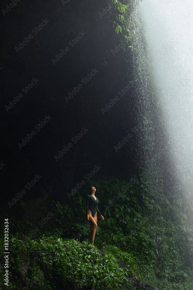 Obraz premium Sexy Woman in Swimsuit Standing Under Dramatic Jungle Waterfall Light