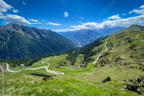 Panoramic view into Passeier Valley (germ. Passeiertal) from Jaufenpass in South Tyrol, Italy with winding mountain road, green pastures and forested slopes under a blue sky
